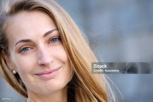 Smiling woman with natural eyebrows and blue eyes.