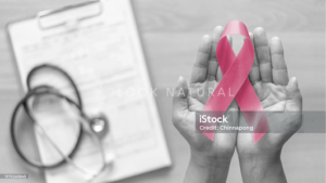 Hands holding a pink ribbon with medical clipboard and stethoscope in background.